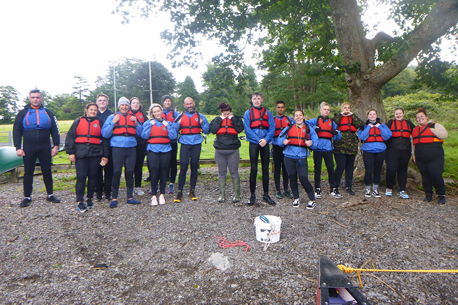 Image description: Young people dressed in wet suits and buoyancy aids, standing on a rocky shore.